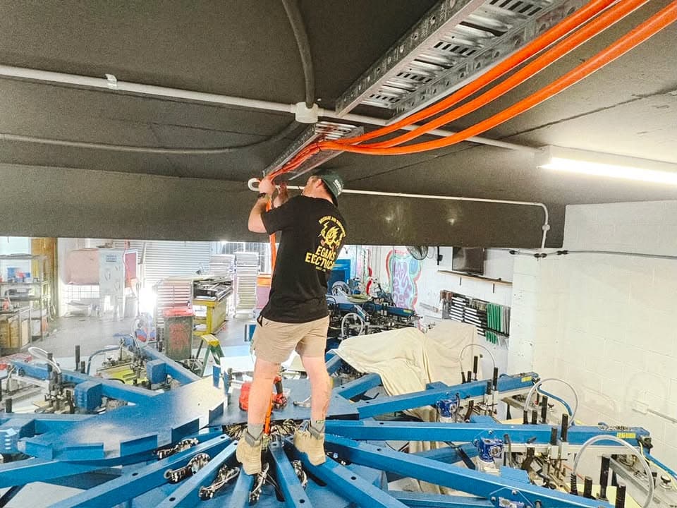 Egans Electrical electrician working overhead on cable containment in a Brisbane workshop